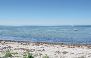 Een strand met kalm water, een verafgelegen vuurtoren en een klein bootje.