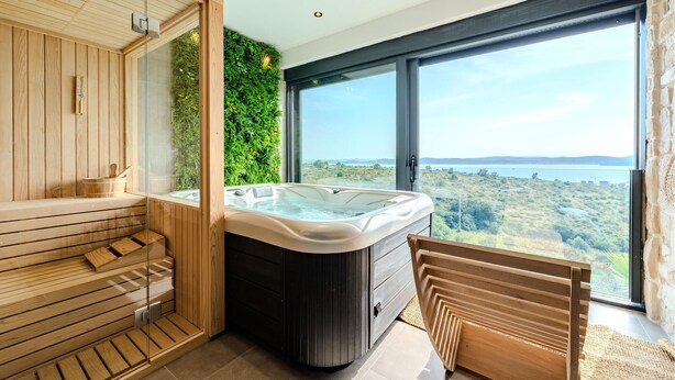 Ein modernes Saunabadezimmer mit Holzvertäfelung, einem Whirlpool und einem großen Fenster mit schöner Aussicht.