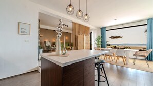 Eine moderne Küche mit Kochinsel, ein Essbereich mit Ausblick und ein Wohnbereich mit Sofa und Pflanzen.