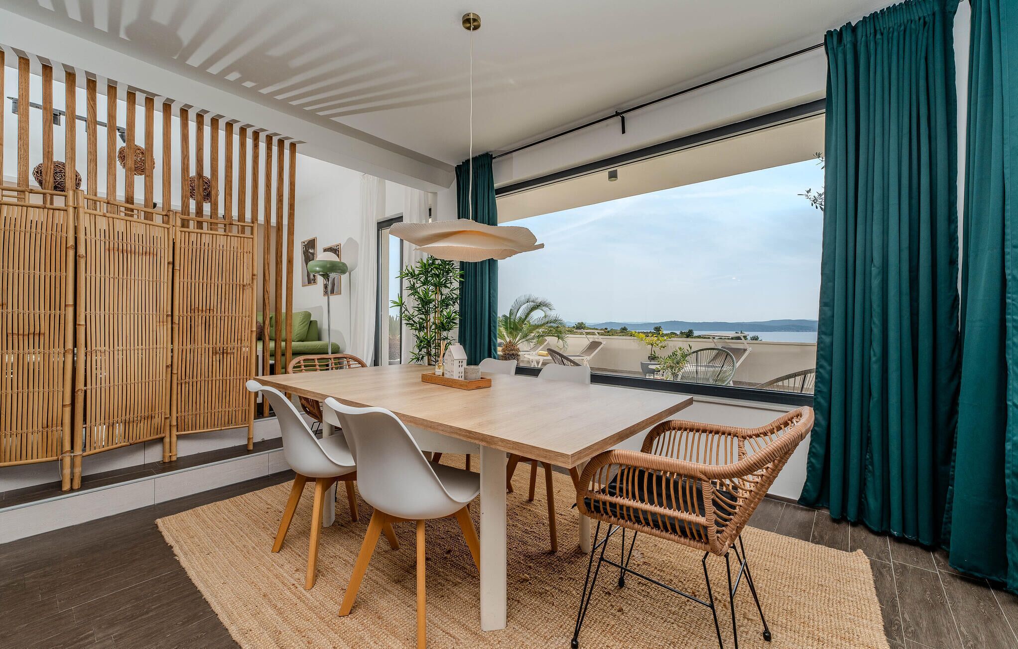 A modern dining area with a wooden table, white chairs, and a view of the sea through large windows.