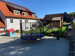 A playground with a trampoline, a slide, and a small house structure.