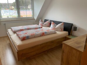 A bedroom with a bed, pillows, a nightstand, a lamp, and a view of buildings outside. - Vacation apartment Lahner (Königsfeld)