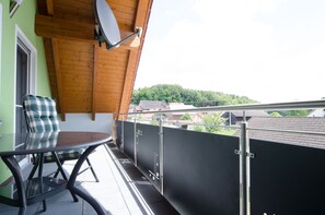 A balcony with a glass table and a plaid cushion, overlooking a residential area with houses and trees. - Vacation apartment Lahner (Königsfeld)