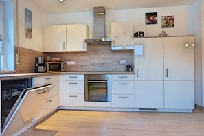 Ett modernt kök med vita skåp, en inbyggd ugn, en mikrovågsugn och en kaffebryggare.