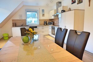 A modern kitchen with a dining area, featuring a large window, white cabinetry, and a dining table with chairs.
