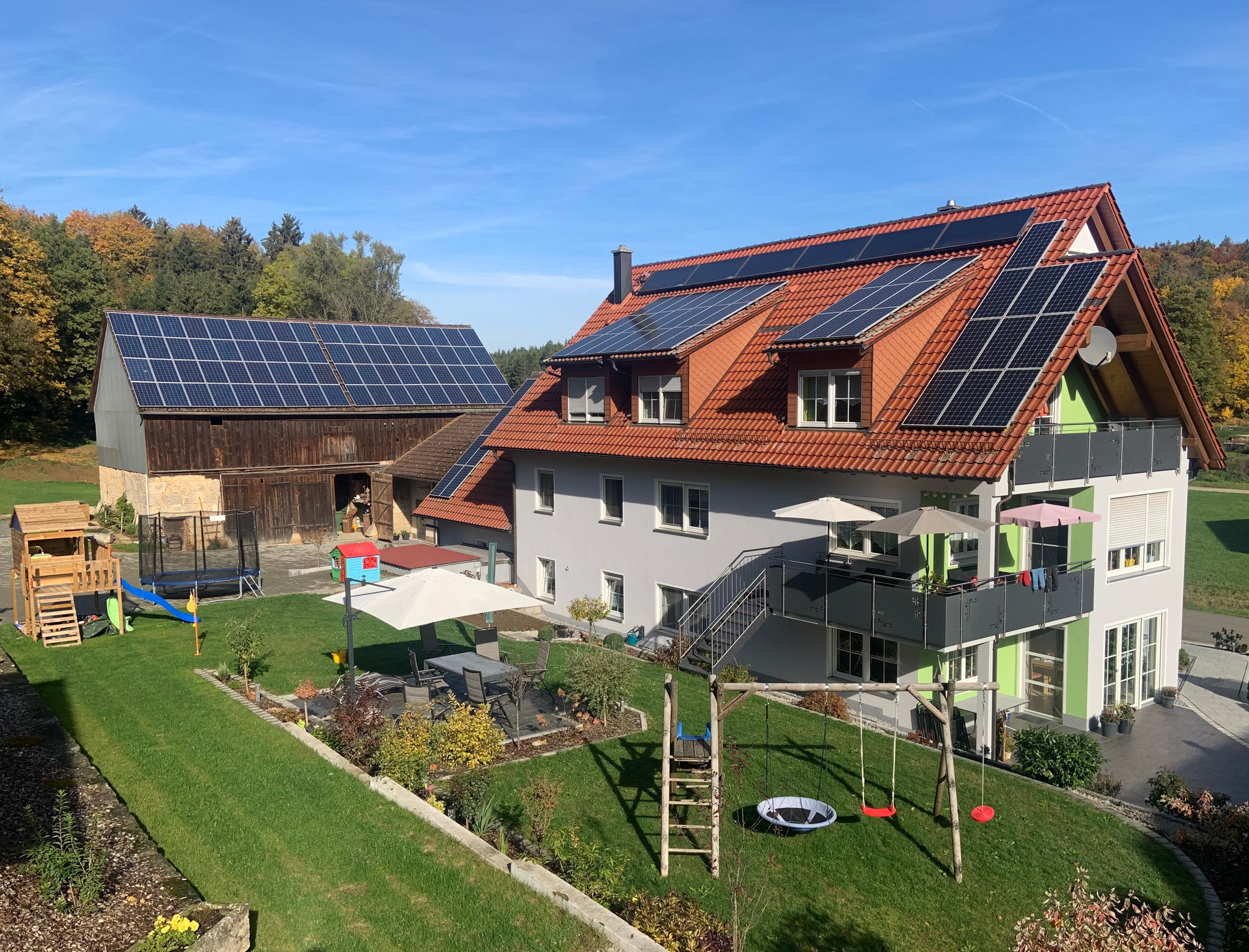 A house with solar panels, a wooden barn, a play area, and a garden.