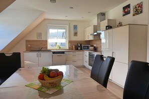 A modern kitchen with a dining table, chairs, and a fruit basket. - Vacation apartment Lahner (Königsfeld)