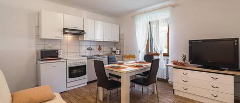 Een compacte keuken met witte kasten, een fornuis en een eethoek met een tafel voor vier personen.