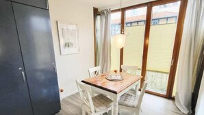 Un coin repas avec une table en bois et des chaises blanches, un buffet sombre et une fenêtre avec des rideaux.