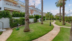 A well-maintained garden with palm trees, a stone pathway, and a white building with balconies. - Cozy apartment in Guardamar del Segura (Guardamar del Segura)