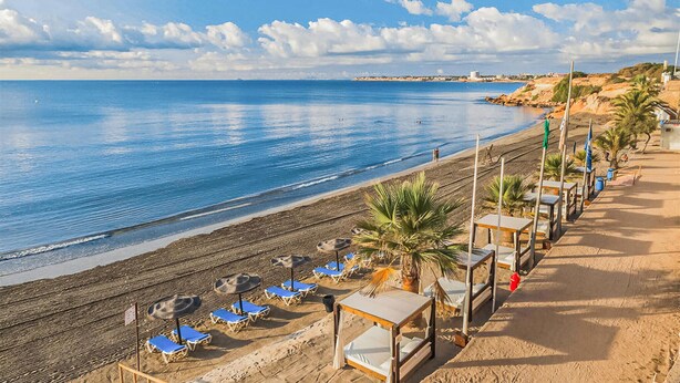 A beach with sun loungers, umbrellas, and a row of wooden cabanas along the shoreline. - Cozy apartment in Guardamar del Segura (Guardamar del Segura)