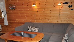 Een knus interieur met een houten wand, een grijze bank, een houten bijzettafeltje met een onderzetter en een geruit kleedje, en twee wandlampen.