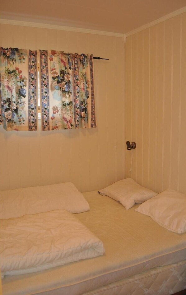 Ein Zimmer mit einem Bett, einem Fenster mit blumigen Vorhängen und einer Tür.