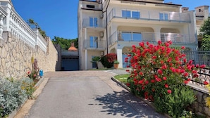 A multi-story building with balconies, a stone wall, and a well-maintained garden with red flowers.