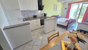 A compact kitchen with white cabinets, a stove, and a sink. There's a dining area with a table and chairs, and a bed with a window view.