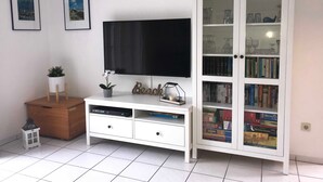 A white entertainment unit with a flat-screen TV, a small potted plant, and a decorative item. - Vacation home in Nessmersiel 20-129a - 200-129a (Dornum)