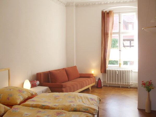 A bedroom with a bed, a sofa, a radiator, and a window with curtains.