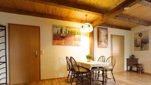 A dining area with a wooden table and chairs, a hanging light fixture, and artwork on the walls. - Apartment 2 - Fewos "Storchenhof" near the lake (Meesiger)