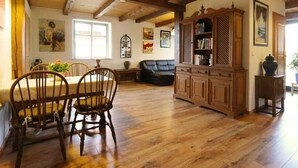 A spacious living room with wooden flooring, a dining area with a table and chairs, a fireplace, and a bookshelf. - Apartment 2 - Fewos "Storchenhof" near the lake (Meesiger)