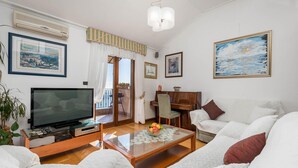 Una sala de estar con televisor, un piano, una mesa de centro de vidrio con fruta y un sofá.