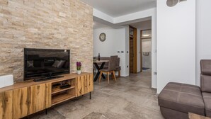 Een moderne woonkamer met een stenen muur, een flatscreen-tv, een houten entertainmentmeubel, een eethoek met tafel en stoelen, en een bruine leren bank.
