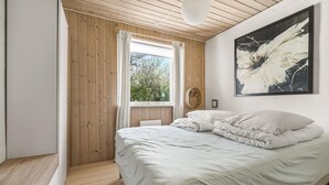 Ein Schlafzimmer mit Holzboden, einem großen Fenster mit Vorhängen, einem Bett mit weißer Bettwäsche und einem modernen abstrakten Gemälde an der Wand.