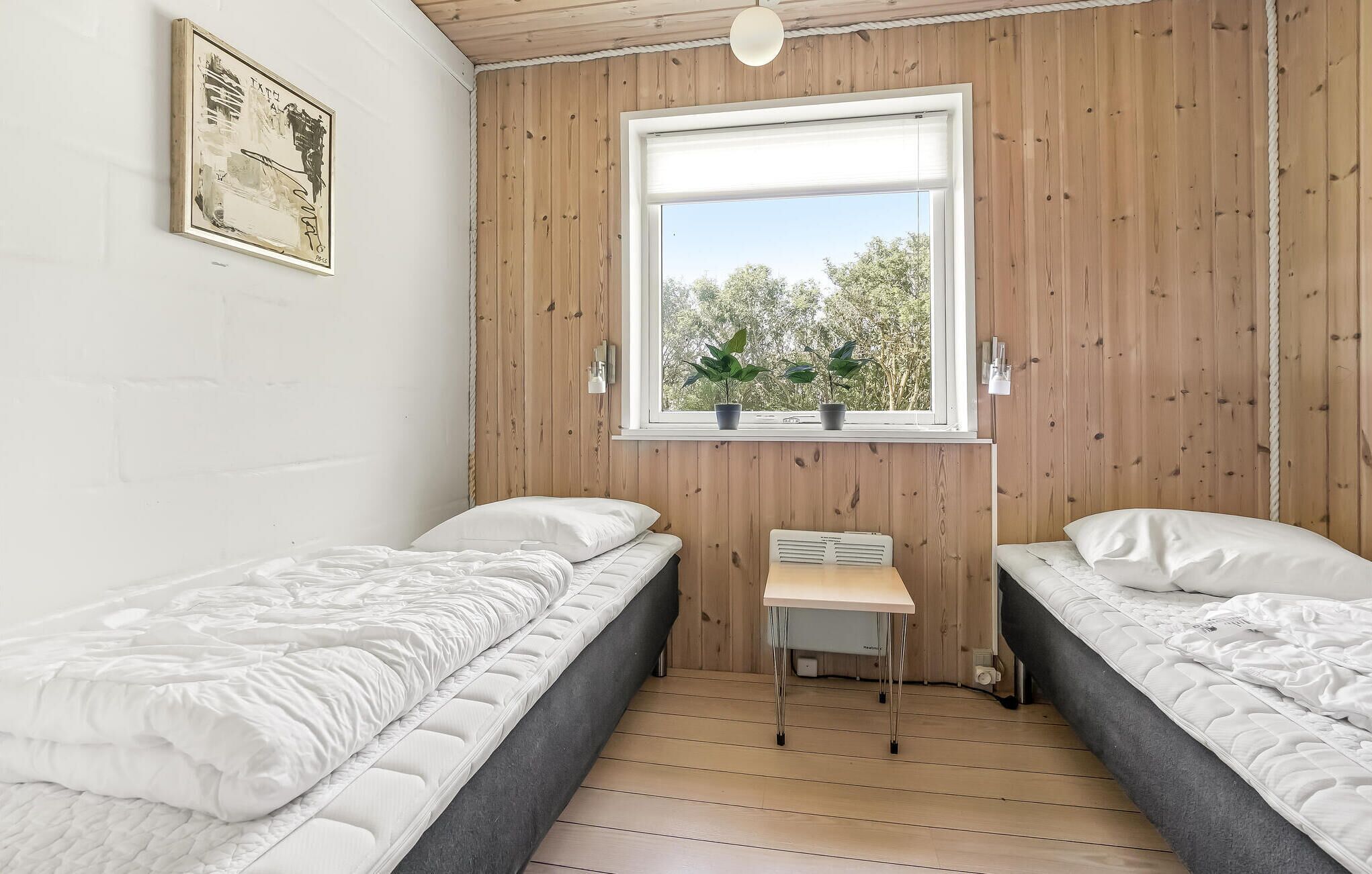 Une petite chambre agréable, dotée de deux lits simples, d’une petite table et d’une fenêtre donnant sur les arbres.
