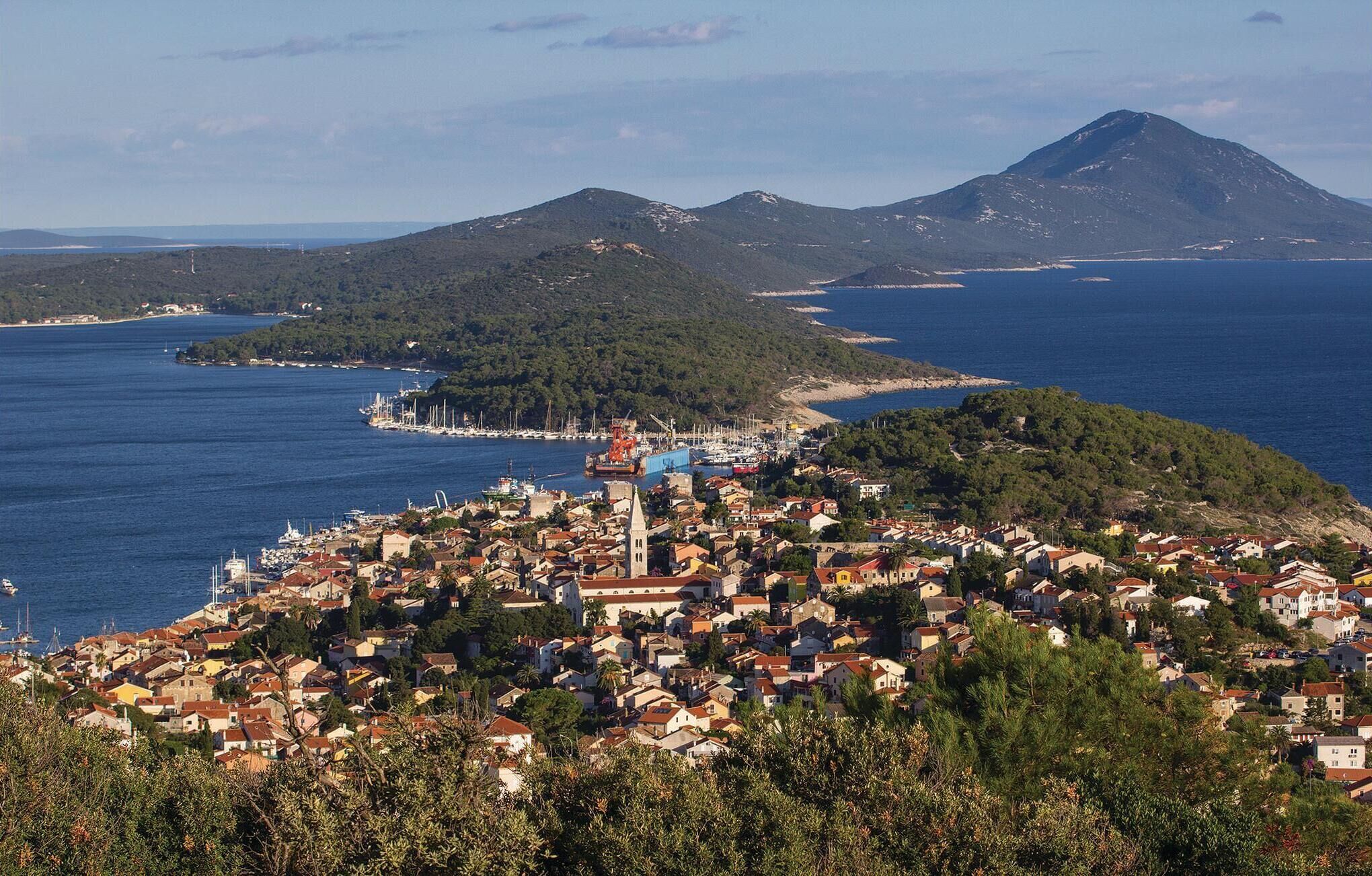 A coastal town with a prominent church, a marina, and a mountain in the background.