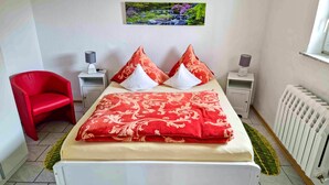 A bedroom with a bed, a red chair, two bedside tables with lamps, a radiator, and a picture on the wall.