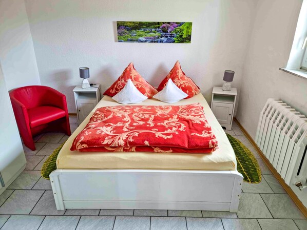 Een slaapkamer met een bed, een rode stoel, twee nachtkastjes met lampen, een radiator en een foto aan de muur.