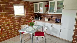 A compact kitchen with white cabinets, a microwave, and a small dining table with a red chair.