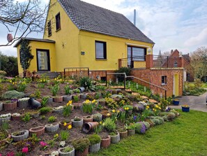 A yellow house with a brick extension, surrounded by a garden with various plants and flowers.