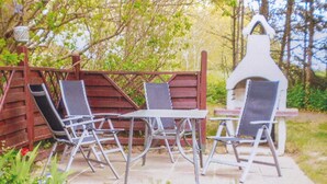 An outdoor patio with a wooden fence, a grill, and a table with chairs.