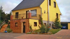 A two-story yellow house with a brick base, a balcony, and a satellite dish.