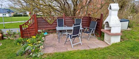 Une terrasse extérieure avec une clôture en bois, un barbecue et un espace détente comprenant des chaises et une table.