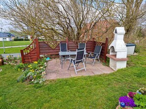 Eine Terrassenanlage im Freien mit Holzlattenzaun, Grill und einer Sitzgruppe mit Stühlen und Tisch.