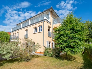 Un edificio di due piani con un balcone, immerso nel verde sotto un cielo sereno.