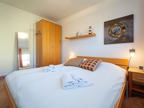 A neatly made bed with towels, a wooden wardrobe, a shelf with decorative items, and a wall clock.