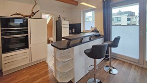 Eine moderne Küche mit Einbauofen und Holzbalkendecke, ein Barbereich mit Hockern und große Fenster mit Blick auf die Stadt.