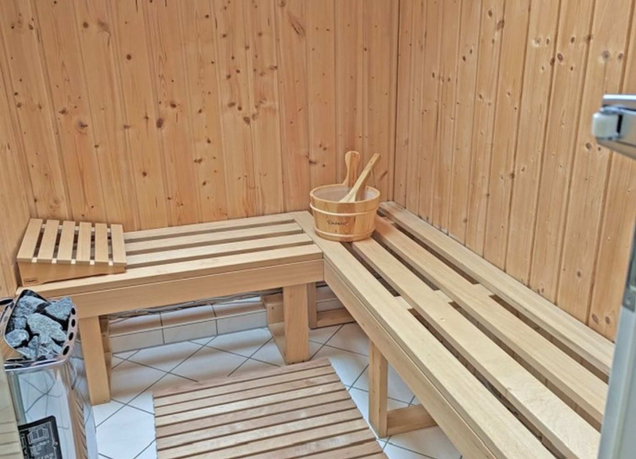 Un sauna en bois, avec des bancs et un seau en bois accompagné d’une louche.