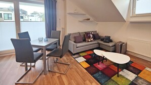 Ein modernes Wohnzimmer mit Essbereich, einem farbenfrohen Teppich und einer schrägen Decke.