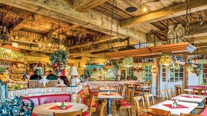 Ein rustikales Restaurant mit Holzbalken, Backsteinwänden und verschiedenen hängenden Dekorationen. Tische und Stühle sind zum Essen aufgestellt.