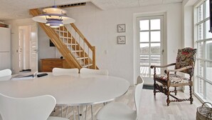Een ruime eethoek met een grote ronde tafel, witte stoelen, een houten trap en een groot raam met uitzicht.
