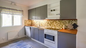Een keuken met grijze kastjes, een betegelde spatwand, een inbouwoven en een raam met gordijnen.
