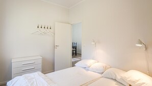 Een slaapkamer met een bed, nachtkastjes, een kledingkast, een hanglamp en een deur naar een andere kamer.