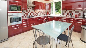 Une cuisine moderne avec des meubles de rangement rouges, une table en verre et deux chaises.