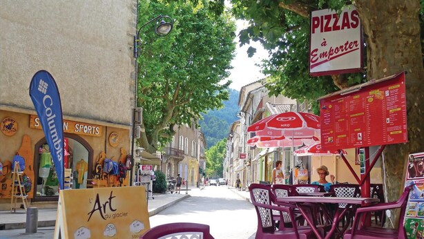 Une rue avec des terrasses, un restaurant de pizzas et un magasin d’articles de sport.
