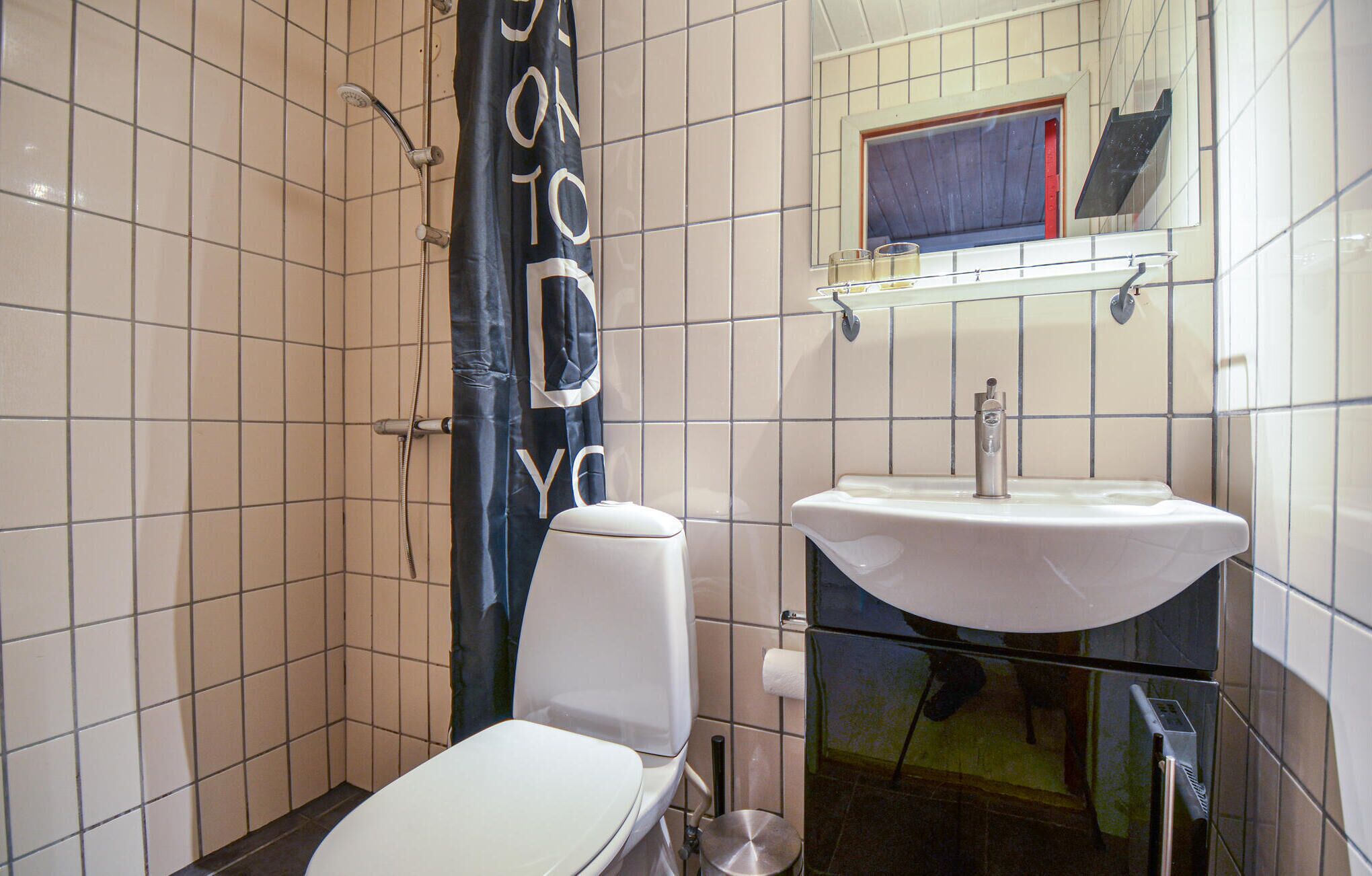 A bathroom with white tiles, a white toilet, a sink with a mirror above it, and a shower curtain with text.
