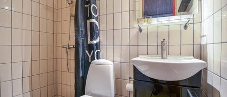 A bathroom with white tiles, a white toilet, a sink with a mirror above it, and a shower curtain with text.