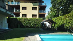 A swimming pool with a paved walkway leading to it, surrounded by a well-maintained lawn and a building with multiple balconies. - Holiday apartment with pool Wi-Fi and tasteful decoration (Siófok)